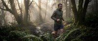 Athletic man jogging through misty forest trail at dawn with sunbeams filtering through trees, outdoor fitness and nature workout concept.