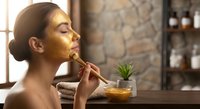 Young woman applying golden face mask with brush in spa setting for skincare and beauty treatment routine.