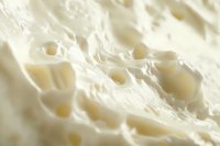 Extreme close-up macro photography of fresh cream cheese texture showing soft white surface with tiny holes and creamy swirls in natural light.