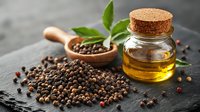 Black peppercorns scattered on dark stone surface with glass bottle of essential oil, wooden spoon and fresh green leaves, moody food styling.