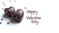 Heart shaped chocolate candies with silver sprinkles and Happy Valentine Day text on white background. Romantic holiday celebration concept with sweet treats and festive decoration.