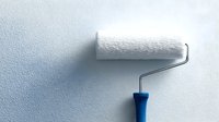 Paint roller with blue handle casting shadow on textured white wall, ready for home renovation and interior painting projects.