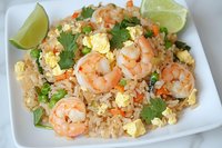 Shrimp fried rice with scrambled eggs, fresh cilantro and lime wedges garnish on white plate, close up view of Asian cuisine dish with tender seafood.
