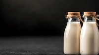 Fresh organic milk in glass bottles with cork stoppers on dark background for healthy dairy products and natural food concepts.