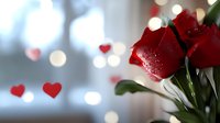 Vibrant red roses with water droplets against blurred bokeh background with heart decorations, creating romantic Valentine's Day atmosphere.