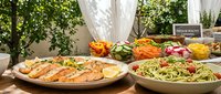 Grilled salmon with herb pasta and fresh salad buffet spread on outdoor patio table for healthy dining and entertaining guests at summer gathering.