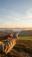 Person stretching arms toward golden sunrise over misty countryside landscape with rolling hills and farmland during peaceful morning meditation.