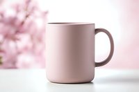 Minimalist pink ceramic mug on white surface against soft blurred floral background. Modern lifestyle product photography for branding and social media.