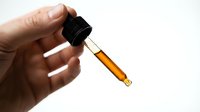 Hand holding glass dropper bottle with amber liquid serum or essential oil against white background for skincare cosmetic product photography.