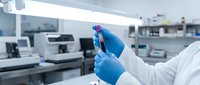 Laboratory scientist in blue gloves holding test tube with red liquid sample in modern medical research facility for scientific analysis and experimentation.