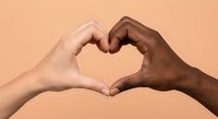 Two diverse hands forming heart shape symbol representing unity love friendship and racial harmony on warm peach background for social campaigns.