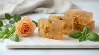 Handmade natural soap bars with oatmeal and rose petals arranged on white plate with fresh orange rose and green leaves for spa and wellness.