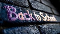 Pink and purple chalk lettering spelling Back to School on dark textured brick wall background with selective focus and dramatic lighting effect.