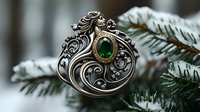 Ornate silver brooch with emerald gemstone and flowing art nouveau design against snowy pine branches, showcasing intricate metalwork and vintage jewelry craftsmanship.
