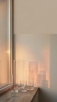 Empty drinking glasses arranged on wooden windowsill with warm sunlight streaming through window, creating soft shadows on beige wall for home decor and interior design projects.