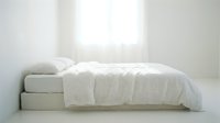 Minimalist bedroom with white bed, crisp linens, and soft natural light from window, conveying calm and clean sleeping space for interior design and lifestyle projects.