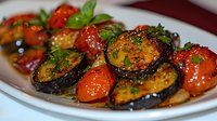 Grilled eggplant slices and cherry tomatoes garnished with fresh basil and seasonings in savory sauce on white ceramic plate, close up view of Mediterranean dish.