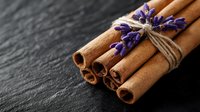 Aromatic cinnamon sticks tied with twine and decorated with fresh lavender flowers on dark slate background, moody food photography composition for culinary designs.