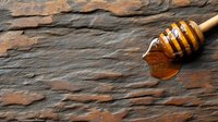 Wooden honey dipper with golden honey dripping on rustic slate stone background. Natural organic sweetener for cooking and baking recipes.