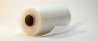 Roll of white bubble wrap with partially unrolled section on neutral background, suitable for packaging, shipping, and protective material concepts.