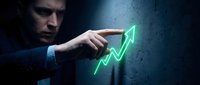Young adult male professional in business attire drawing upward trending neon green arrow on dark textured wall, symbolizing growth, success, and financial progress in corporate environment.