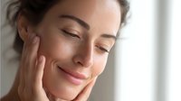 Young woman with glowing healthy skin touching her face gently with closed eyes, expressing wellness, beauty and skincare routine in soft natural lighting.