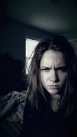 Young woman with long dark hair and pale complexion displaying angry, frustrated expression in dimly lit interior space with window light. Suitable for mental health, emotion, psychology, and dramatic storytelling projects.