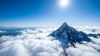 Majestic snow-capped mountain peak rising above white fluffy clouds under bright blue sky. Aerial view of alpine summit for adventure and nature concepts.