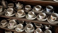 Vintage porcelain tea cups and saucers collection displayed on wooden shelves. Antique floral pattern dinnerware set for elegant dining and hospitality service.