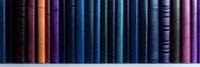 Colorful book spines arranged in row showing gradient from orange to blue and purple tones, creating minimalist library composition with vintage hardcover volumes.