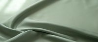 Soft sage green silk fabric with elegant flowing folds and smooth texture for luxury fashion design and textile projects.