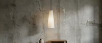 Minimalist pendant lamp with frosted glass shade hanging above wooden furniture against weathered concrete wall, suitable for modern interior design and home decor projects.