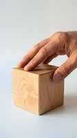 Hand of an adult male placing a natural wooden cube on a white surface, concept of construction, craftsmanship, and geometry.
