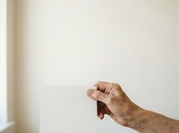 Senior adult hand holding blank white card against neutral wall background for messaging and communication concepts.