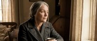 Senior Caucasian businesswoman in gray suit sitting at wooden desk in elegant office interior with natural lighting from window blinds for corporate concepts.
