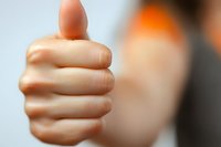 Close-up view of a thumbs up hand gesture against blurred background showing approval, success, and positive feedback in business or social settings.