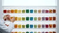 Laboratory technician in white coat organizing colorful samples in glass vials on shelves for scientific research and analysis in modern medical facility.