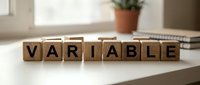Wooden letter blocks spelling VARIABLE on white desk with notebook and plant in background for business concepts and data analysis presentations.