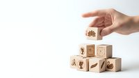 Hand placing wooden cube with leaf symbol onto stack of eco-friendly blocks featuring nature icons on white background for sustainable business concepts.