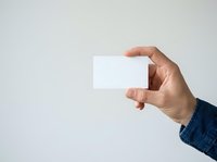 Adult male hand in denim sleeve holding blank white business card against neutral background. Suitable for branding, corporate identity, and marketing mockup designs.