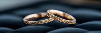 Elegant rose gold wedding rings with delicate Celtic pattern engraving resting on smooth dark stones, showcasing intricate metalwork detail in soft lighting.