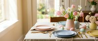 Elegant spring table setting with pastel dinnerware, fresh tulips in vase, and natural lighting for dining room decor and entertaining occasions.