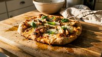 Freshly baked pizza with melted cheese, caramelized onions, and green herbs on wooden board in kitchen setting for food photography and culinary content.