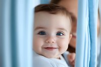 Smiling baby with bright blue eyes peeks through light blue curtains, creating tender moment filled with joy and innocence. Soft natural lighting enhances gentle expression.