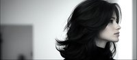 Young Asian woman with flowing dark hair in dramatic black and white profile portrait, showing elegant features and natural beauty against minimalist background.