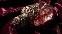 Ornate vintage perfume bottle with intricate golden filigree cap on luxurious burgundy velvet fabric for elegant fragrance and beauty concepts.