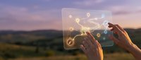 Hands holding transparent tablet with glowing network connections and digital icons against sunset landscape background for technology and connectivity concepts.