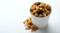 Chocolate granola with nuts and dried fruits in white cup on clean background for healthy breakfast and snack concepts.