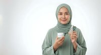 Young Muslim woman in green hijab holding smartphone and credit card for online shopping and digital payments on white background.