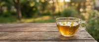 Glass cup of herbal tea on wooden table with blurred garden background. Natural lighting creates warm atmosphere for relaxation and wellness concepts.